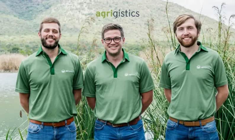 Three Agrigistics founders wearing green branded shirts standing outdoors in a field
